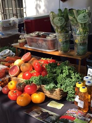 A table with various vegetables and fruits, including heirloom tomatoes, herbs, and grapefruit