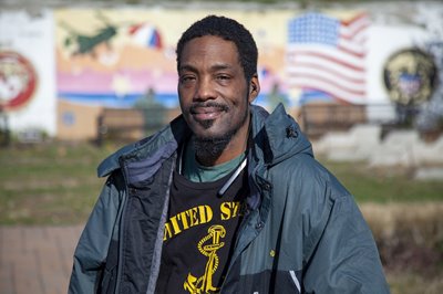 Michael Sanders smiles at the camera with an American Flag in the background.