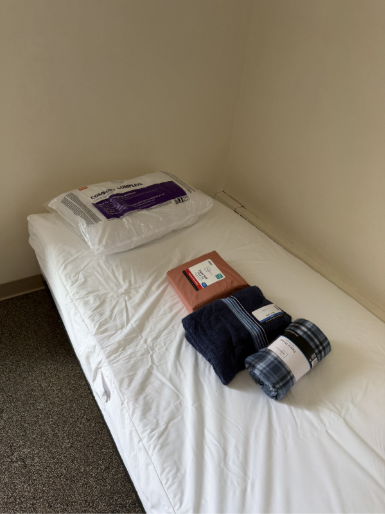 A bed is laid out with sheets and a blanket,, part of a "move-in" kit.
