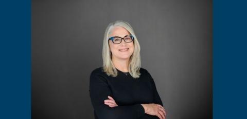 Lee Anne Adams, with her arms folded, against a gray backdrop.